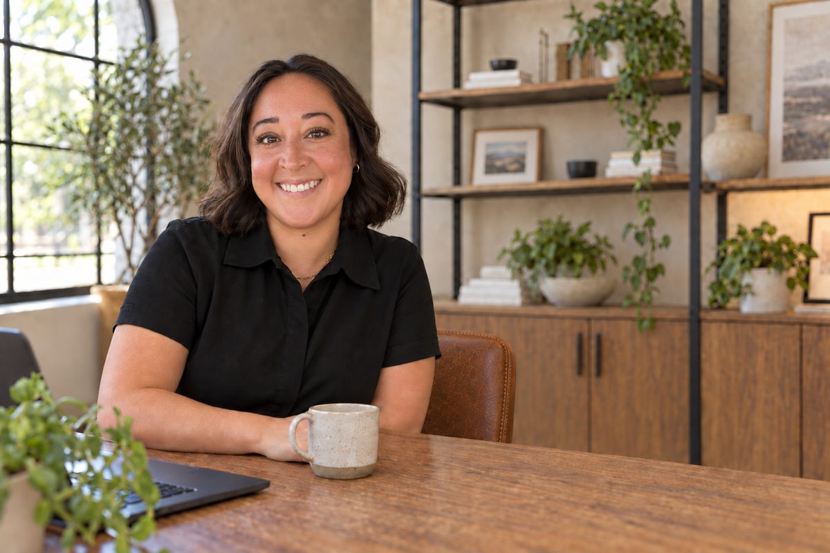 Angela Preciado smiling at her desk with a coffee mug